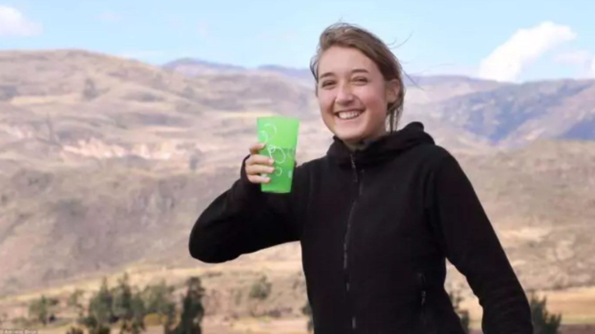 Mujer sonriente bebiendo agua durante una sesión de limpieza digestiva previa al retiro en Cusco, con un paisaje montañoso de fondo.