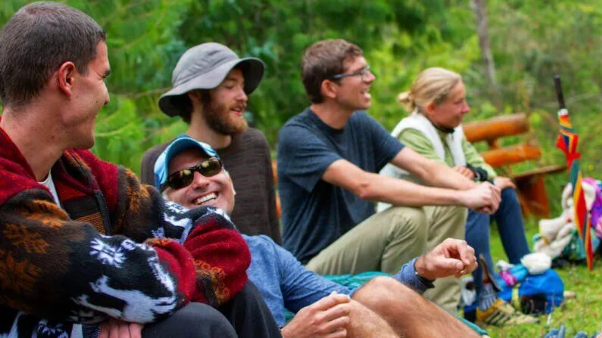 Group of people sitting together outdoors, smiling and engaging in an ancestral medicine session surrounded by nature.