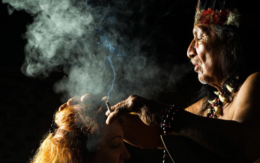 Indigenous shaman performing a spiritual healing ceremony using sacred smoke on a participant's head, promoting energy cleansing and spiritual connection.