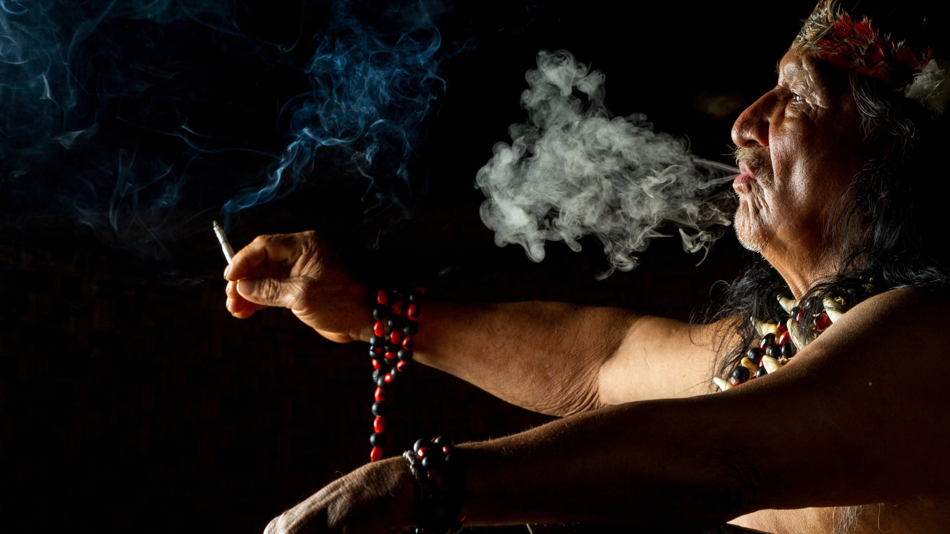 Indigenous shaman performing a ritual ceremony, blowing sacred smoke as part of traditional spiritual practices.