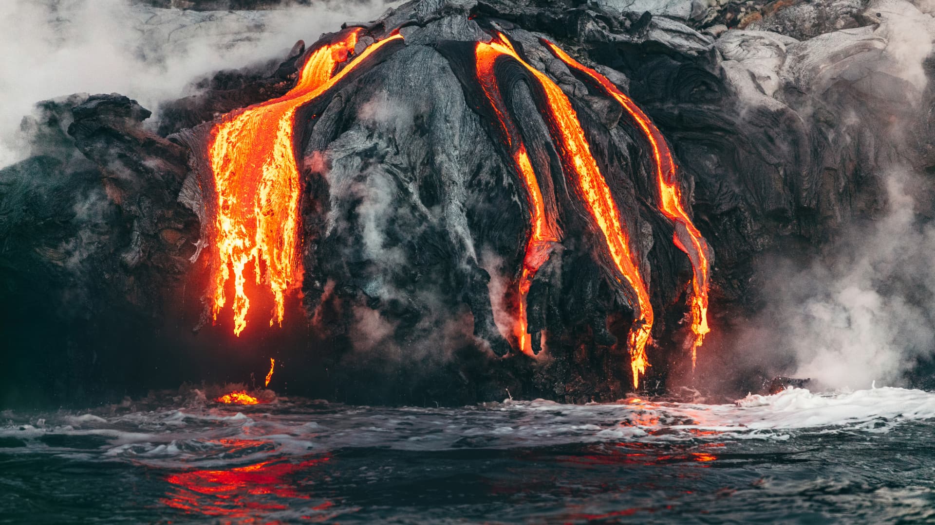 Molten lava flowing from volcanic rock into the ocean, generating steam upon contact with the water.