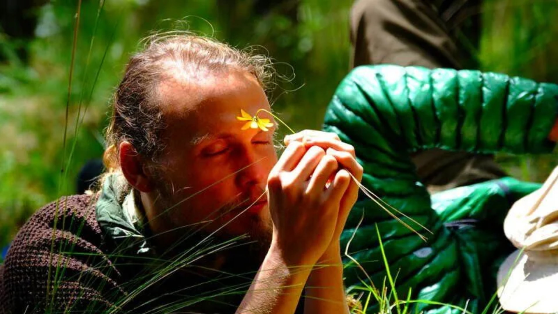 Person holding a yellow flower to their forehead, eyes closed in deep reflection, during an ancestral medicine session outdoors.