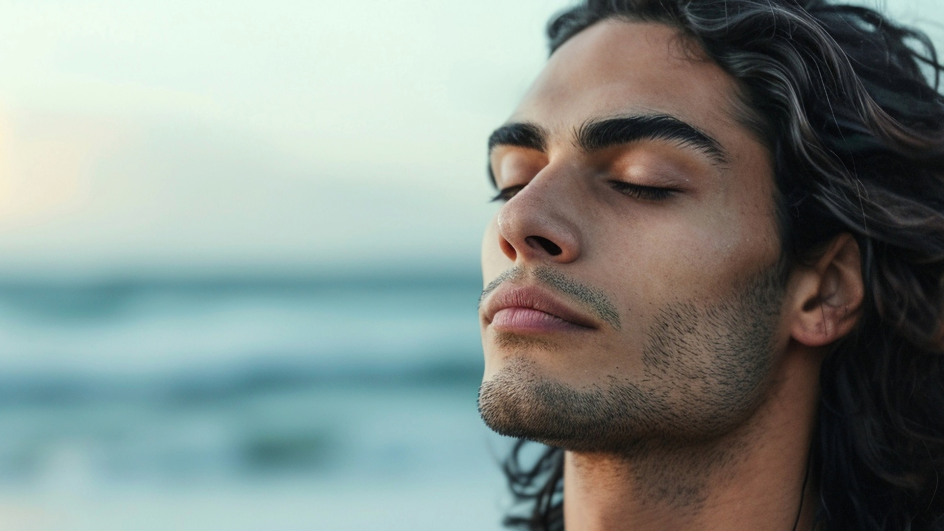 Close-up of a man with eyes closed, meditating peacefully by the ocean, symbolizing tranquility and mindfulness.