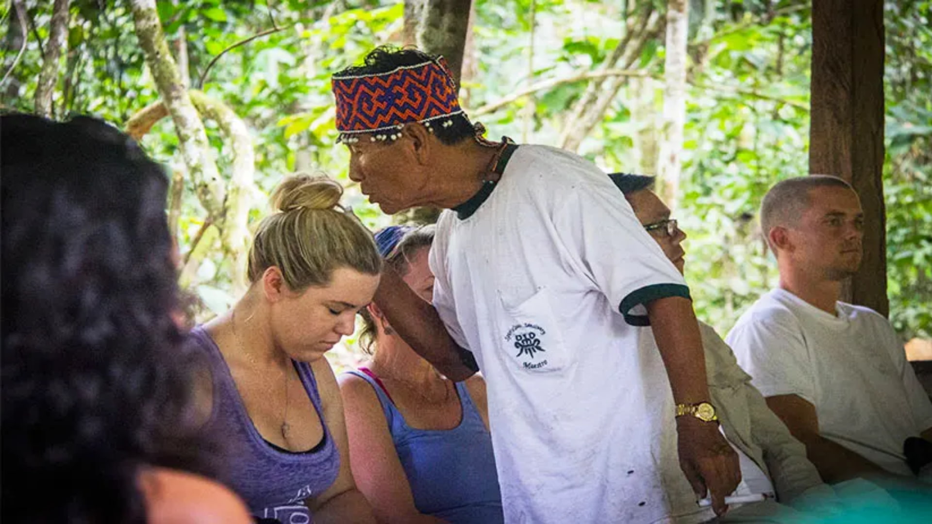 Chamán realizando una ceremonia de sanación espiritual con un participante en un retiro de bienestar en la selva amazónica, rodeado de naturaleza.