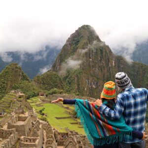 Couple dressed in traditional Andean attire, admiring the scenic view of Machu Picchu ruins with mist-covered mountains in the background, symbolizing adventure and cultural appreciation.