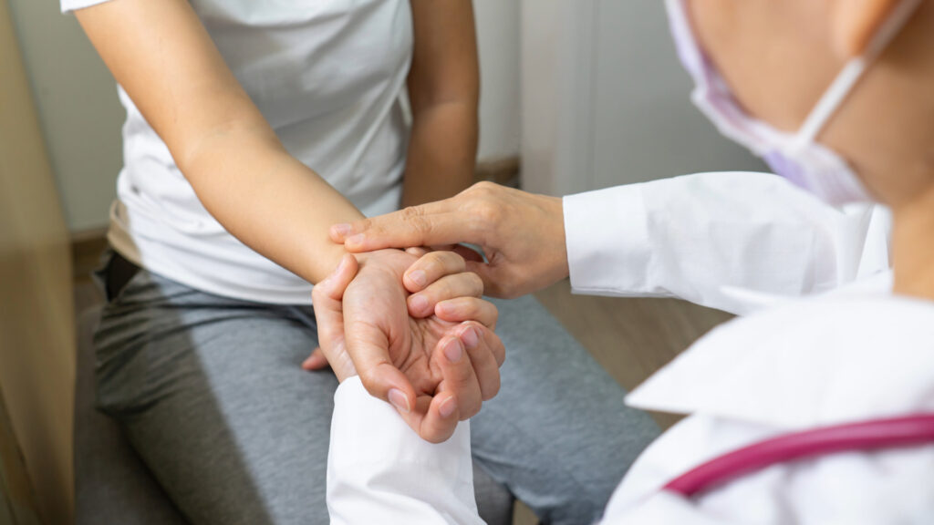 Doctor holding a patient’s wrist to check their pulse during a medical examination, emphasizing patient care and attention to vital signs.