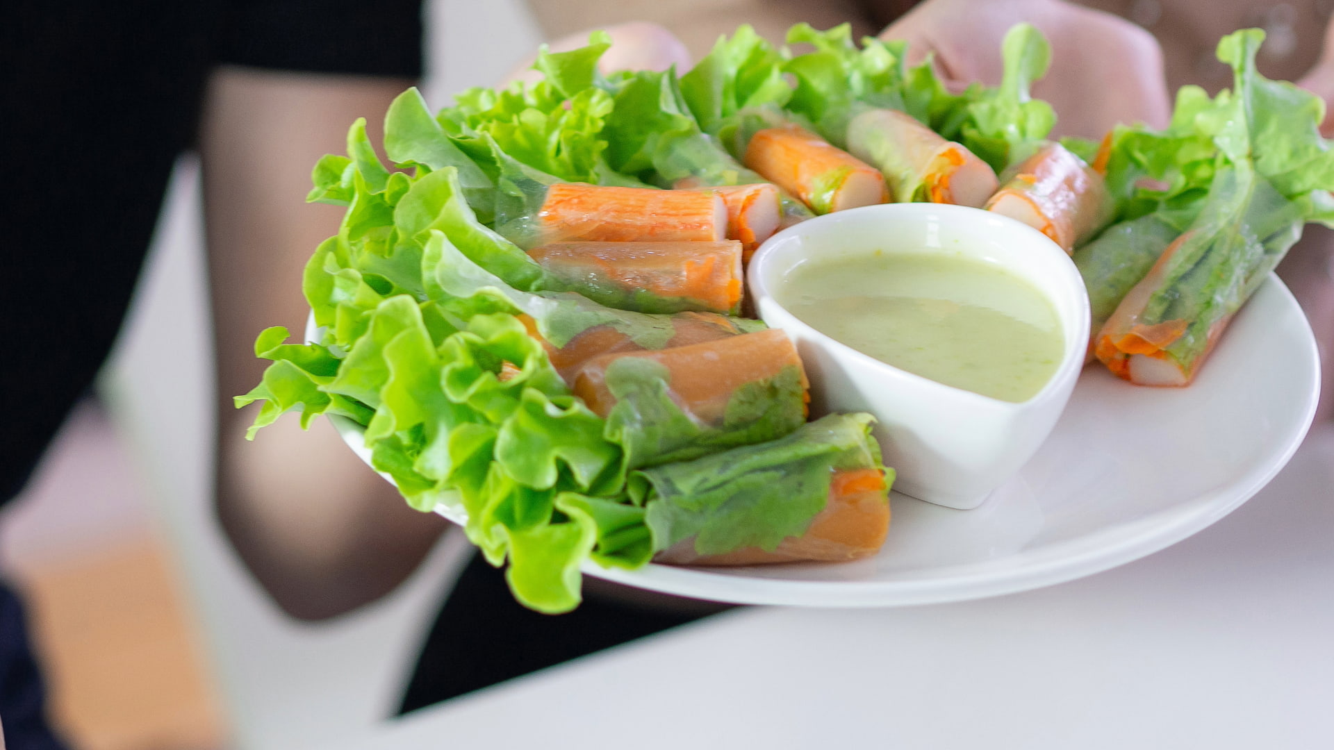 Plate of fresh vegetable spring rolls with lettuce, served with a side of creamy dipping sauce.