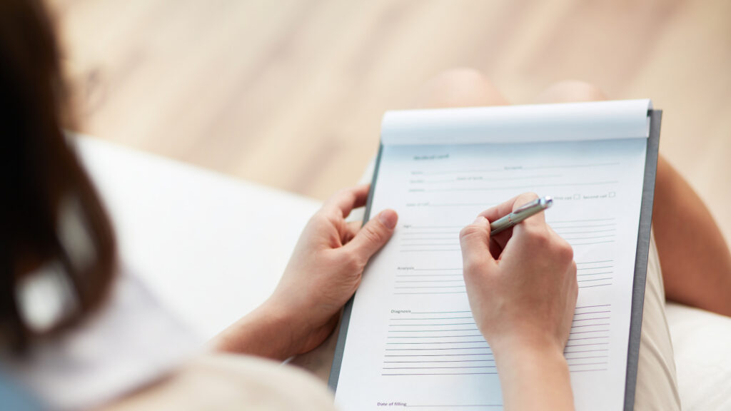 Patient holding a pen and filling out a medical form, highlighting the process of documentation and information gathering in healthcare.