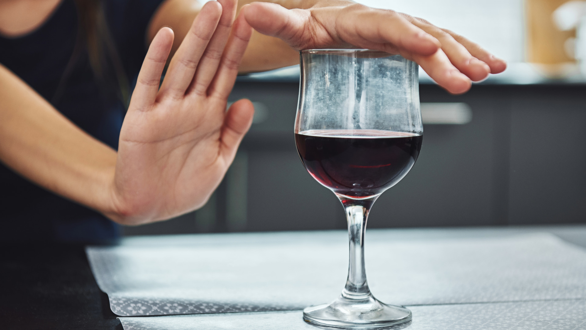 Close-up of a hand signaling "no" to a glass of red wine, representing a choice to abstain from alcohol and promote health and wellness.