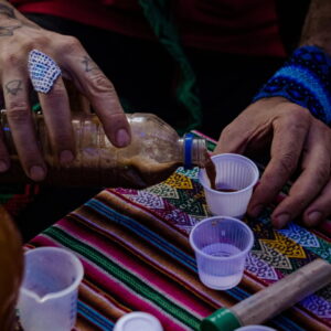 Close-up of hands pouring ayahuasca into small cups during a sacred ceremony, set on a colorful Andean cloth. A moment of cultural and spiritual preparation.