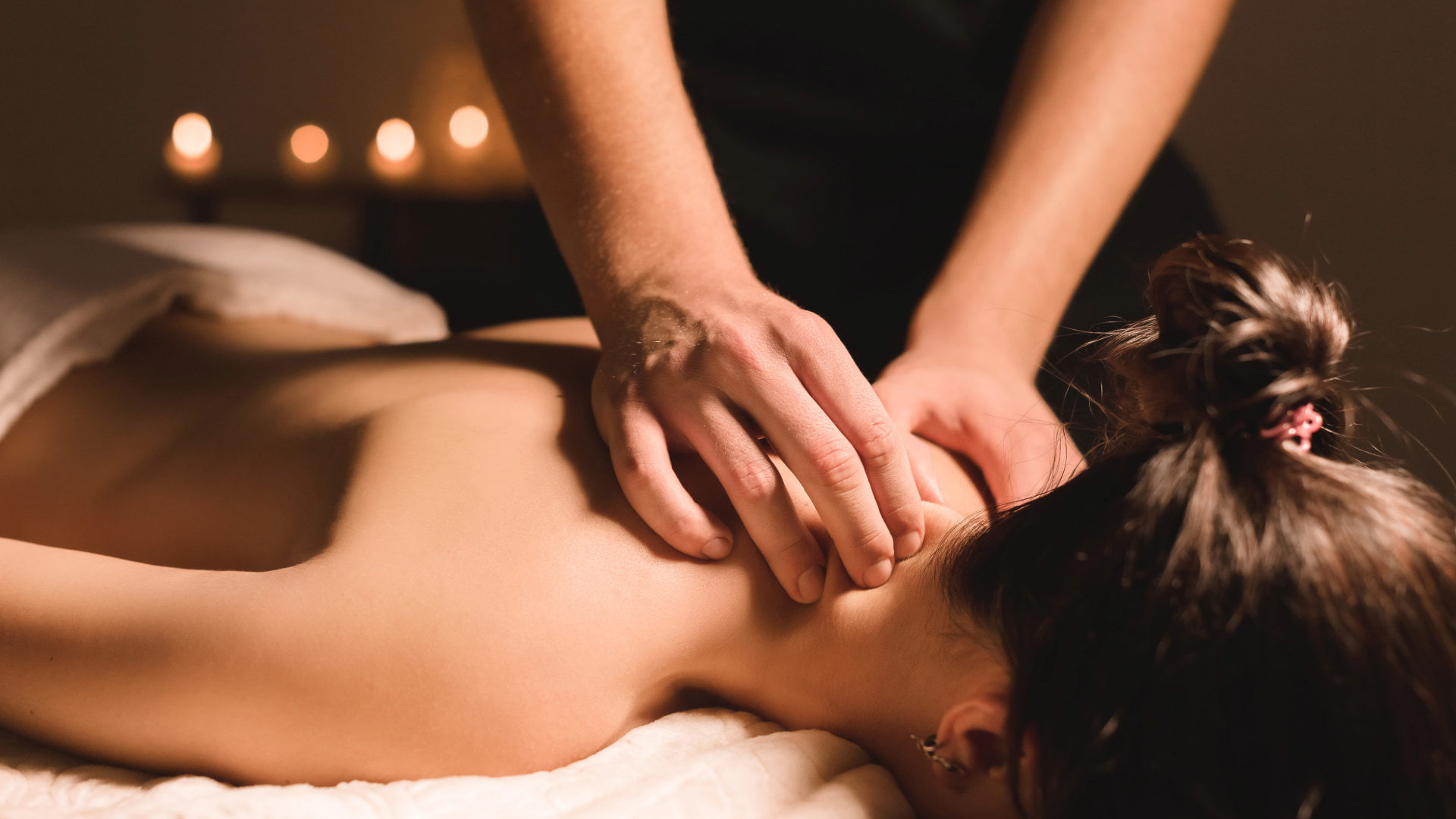 Person receiving a shoulder and neck massage in a calm setting with soft lighting and candles, designed for deep relaxation and stress relief.