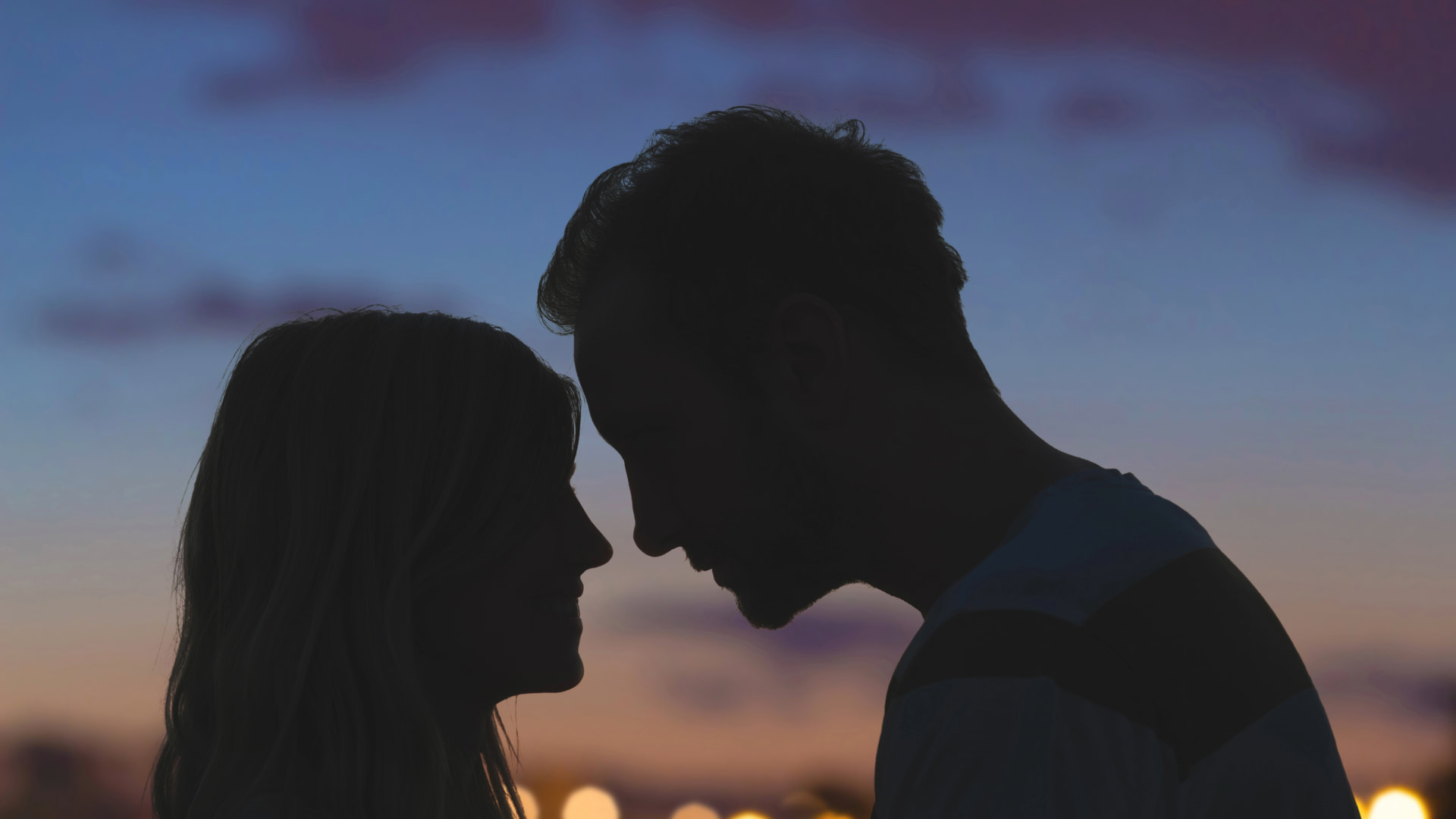 Silhouette of a man and woman facing each other closely, with a soft sunset sky behind them, capturing a romantic and peaceful moment.