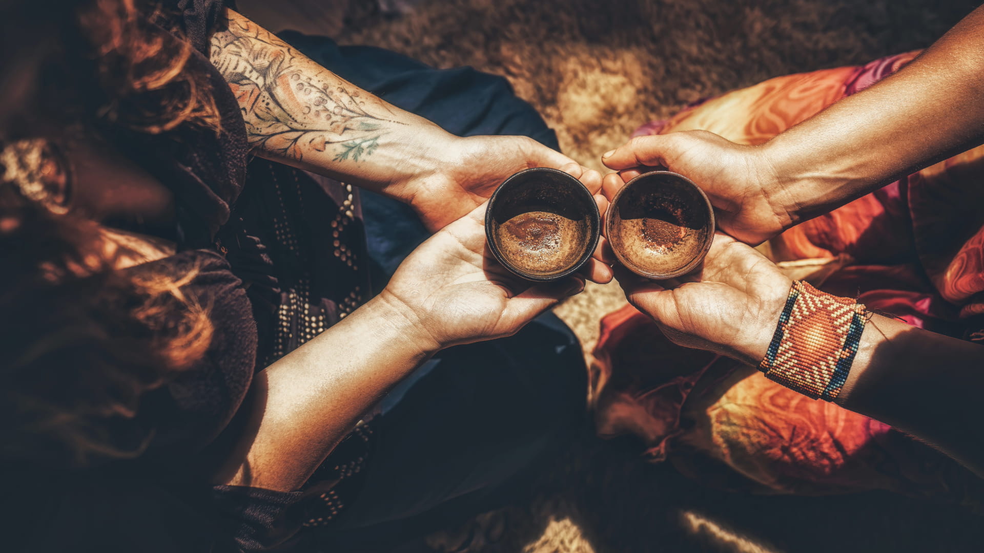 Hands of two people holding ceremonial cups together, creating a moment of connection in a spiritual ritual setting.
