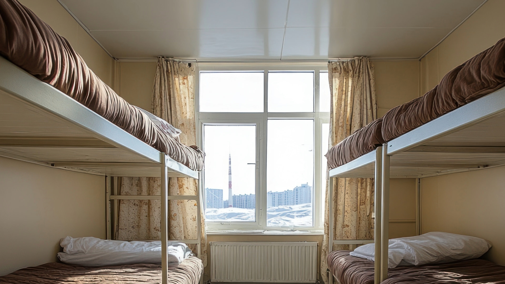 Hostel dorm room with two sets of bunk beds and a large window offering a view of the city.