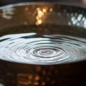 A singing bowl filled with water, showing ripples on the surface, symbolizing calm and healing energy in a meditative setting.