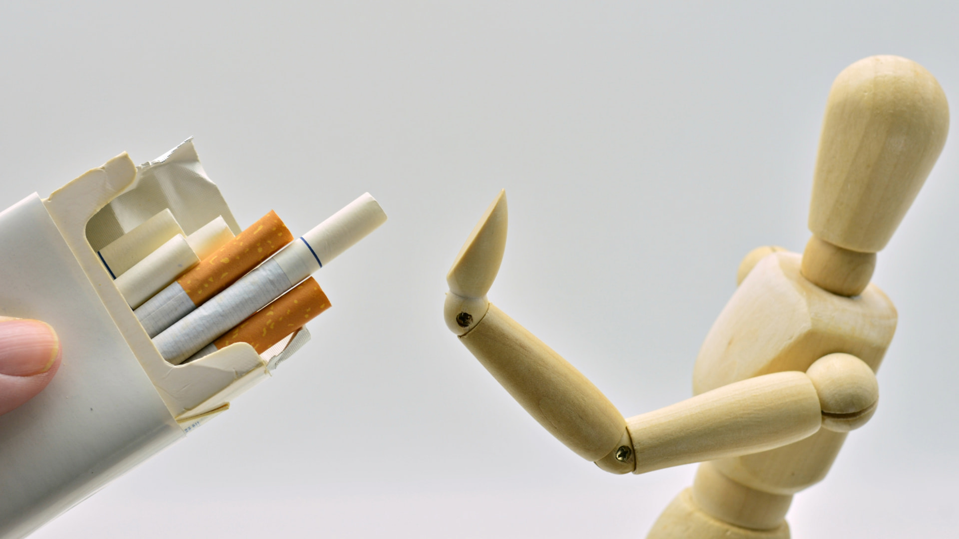 Wooden mannequin with an outstretched hand in a gesture of refusal, turning away from a hand offering a pack of cigarettes, symbolizing anti-smoking or health-conscious decisions.