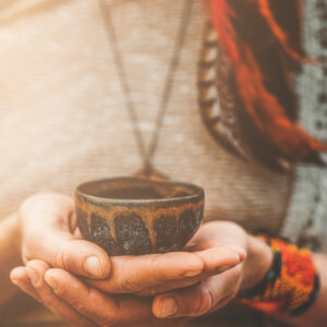 Hands holding a ceremonial cup during a Wachuma ceremony, with traditional clothing elements and a warm, mystical atmosphere.