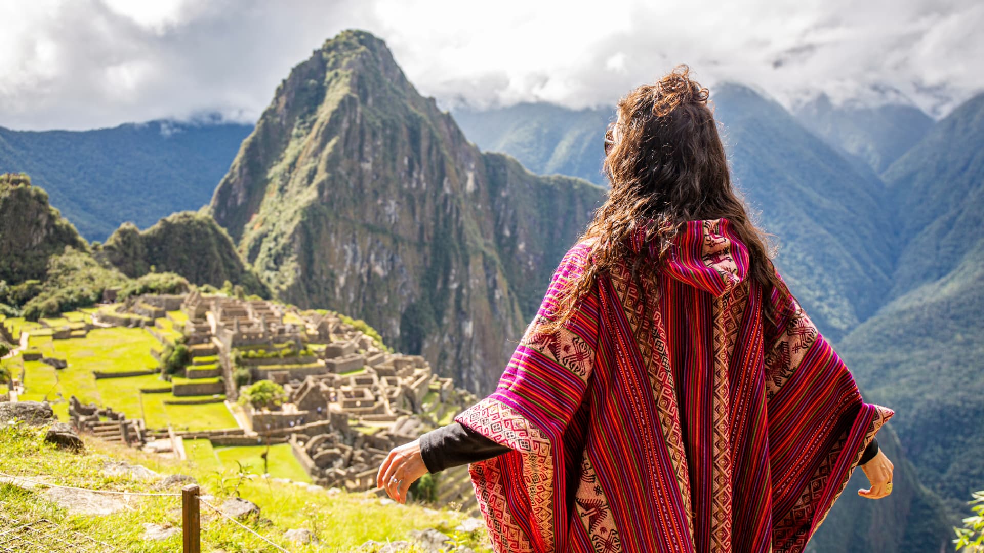 Woman in a vibrant traditional poncho gazing at the ancient ruins of Machu Picchu with misty mountains in the background, symbolizing cultural connection and appreciation of nature's beauty.